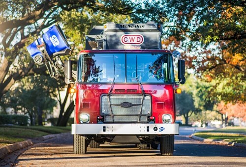 An Autocar ACX severe duty side loader garbage truck picking up trash in a residential street.